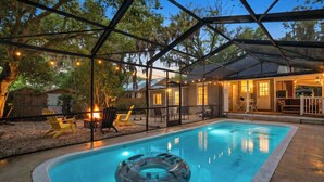 Une piscine dotée d’une enceinte en verre, entourée de mobilier d’extérieur et illuminée de guirlandes lumineuses.