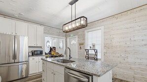Une cuisine moderne avec des armoires blanches, des appareils en acier inoxydable, des comptoirs en granit et un plancher en bois.