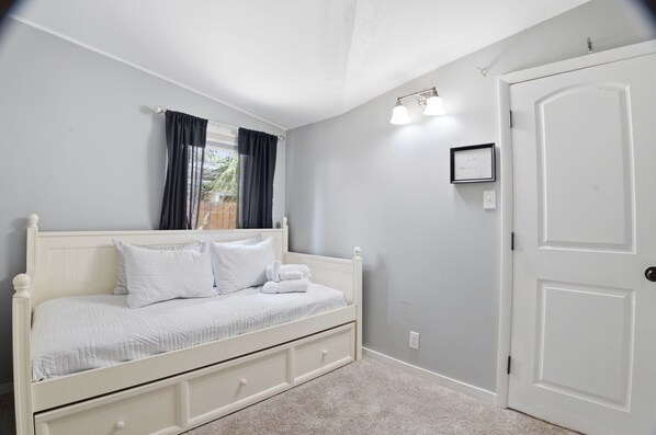 A bedroom with a bed, a door, and a window with curtains.