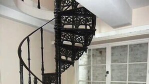 A black spiral staircase with ornate railings in a room with a white radiator and a window with multiple panes. - COTTAGE NIAGARA DIRECT WATERFRONT  (Lincoln)