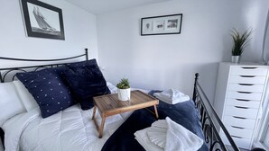 A neatly made bed with a white and navy blue duvet, a wooden bedside table with a plant, and a white dresser with multiple drawers. - COTTAGE NIAGARA DIRECT WATERFRONT  (Lincoln)