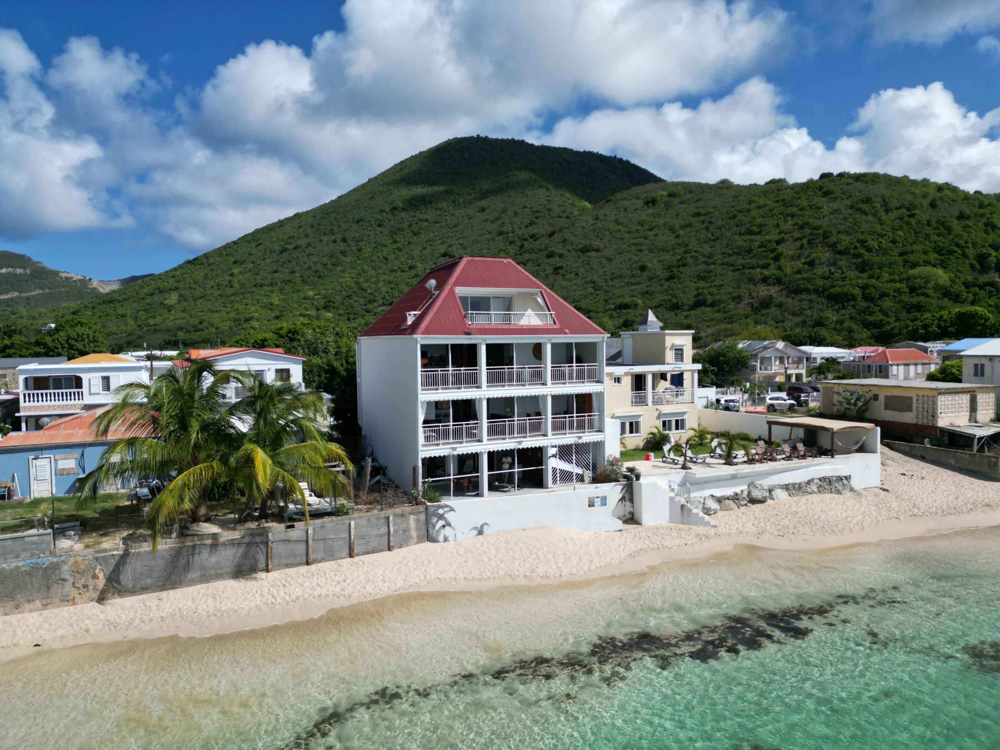 A beachfront property with a two-story building, a sandy beach, and a mountain in the background.