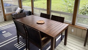 Een houten terras met een eettafel en stoelen, grote ramen met uitzicht op een gazon.