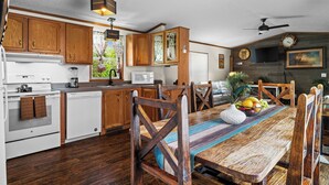Una cocina con armarios de madera, una mesa de comedor con sillas, un microondas y un reloj en la pared.