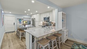 A modern kitchen with white cabinets, a central island with stools, stainless steel appliances, and a patterned rug. - Beautiful Pointe Santo Overlooking Gulf (Sanibel)