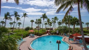 A pool surrounded by palm trees and lounge chairs, with a view of the ocean. - Beautiful Pointe Santo Overlooking Gulf (Sanibel)