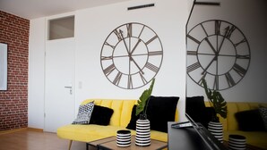 Una sala de estar moderna con un sofá amarillo, dos jarrones a rayas negras y blancas, y dos grandes relojes de pared.