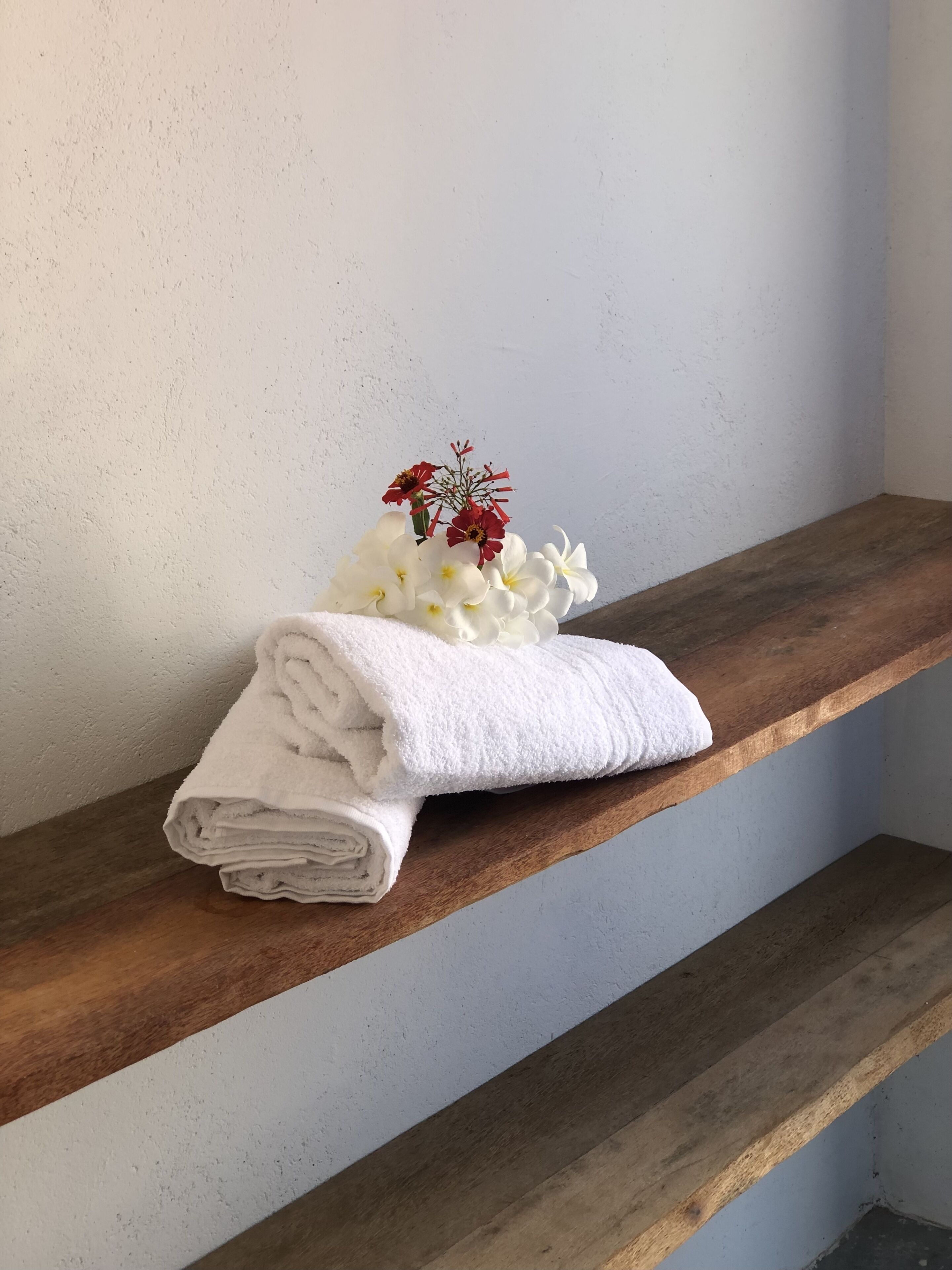 Uno scaffale di legno con un asciugamano bianco piegato e un piccolo bouquet di fiori.