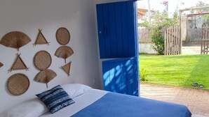Une chambre à coucher avec un lit, une couvre-lit bleue et blanche, un oreiller bleu et blanc et une couverture bleue et blanche. Il y a une fenêtre avec des volets bleus, une vue sur un jardin et un luminaire suspendu.