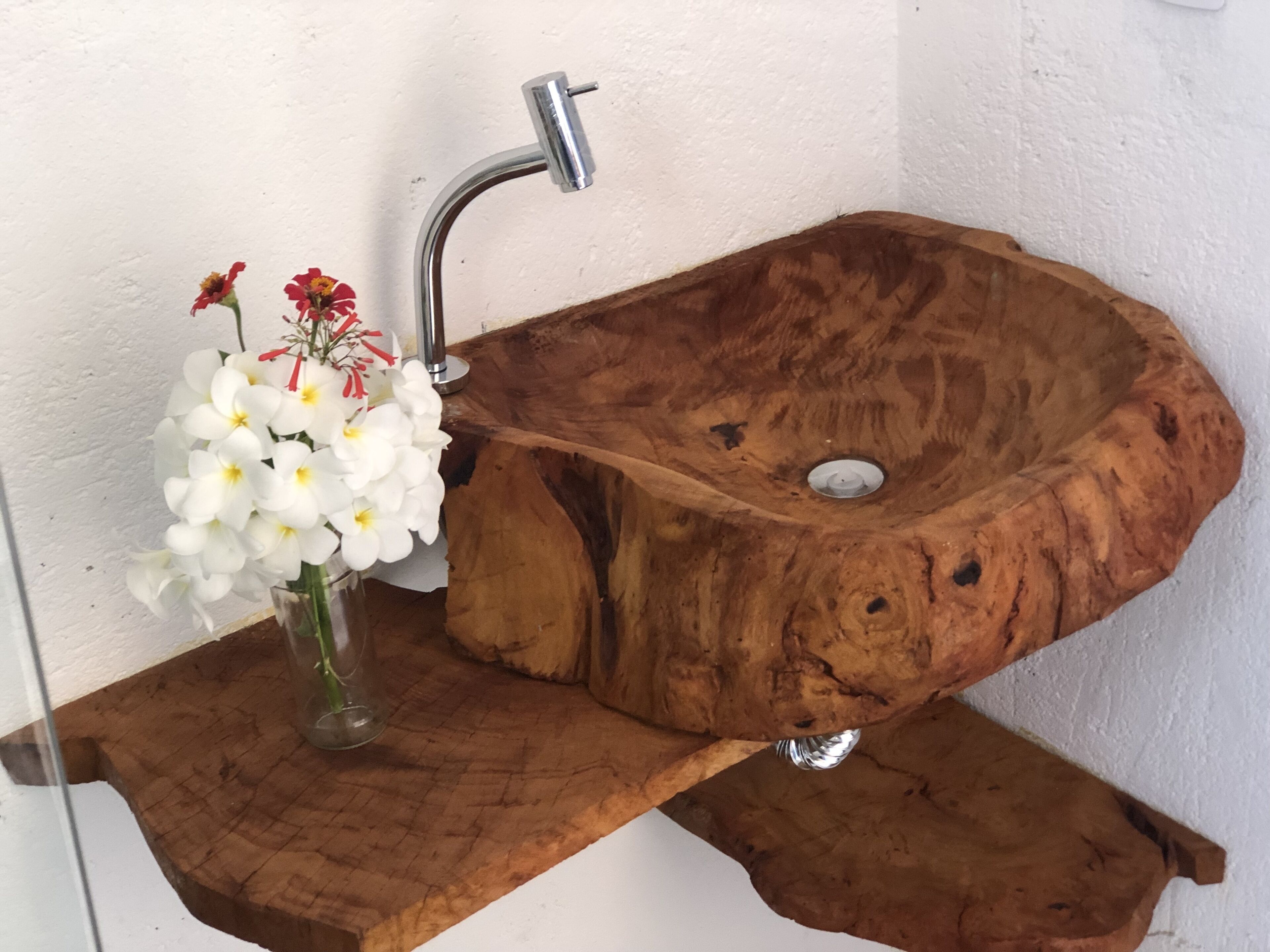 Un lavabo de madera con un grifo moderno y un jarrón con flores blancas sobre un estante de madera.