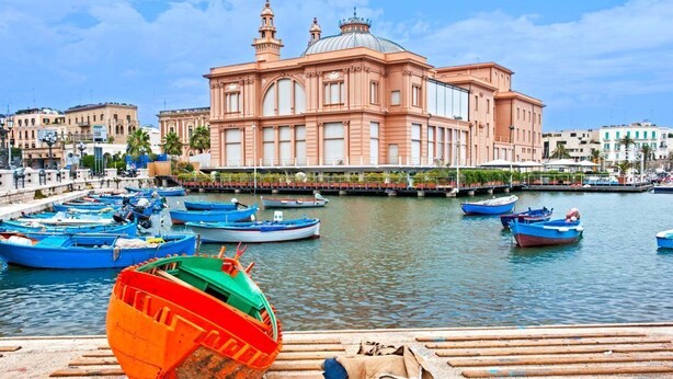A waterfront with boats docked and a prominent pink building with domed roof in the background.