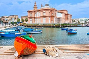 Una banchina con barche ormeggiate, un grande edificio rosa con cupole e una fila di edifici più piccoli lungo la riva.