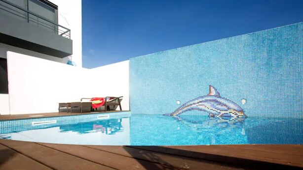 A swimming pool with a dolphin mosaic tile design, wooden deck, and a chair with a red towel. - 2Stay - A1 Local Accommodation with swimming pool (Ponta Delgada)