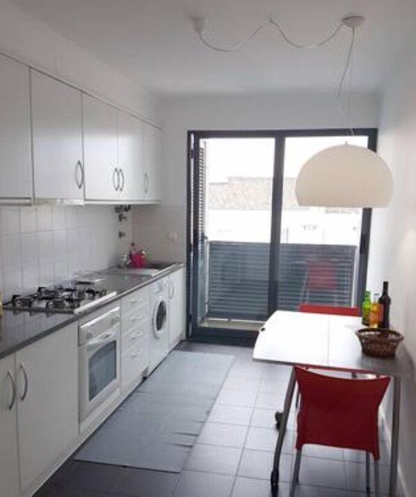 A compact kitchen with white cabinets, a gas stove, a washing machine, and a dining area with a red chair and table. - 2Stay - A1 Local Accommodation with swimming pool (Ponta Delgada)