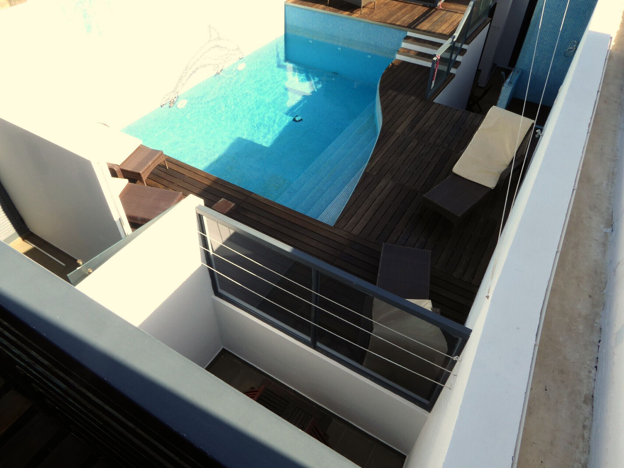 A rooftop pool with a wooden deck and a glass balustrade.