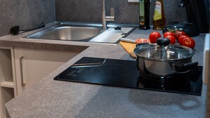 Una cocina moderna con un lavamanos de acero inoxidable, una estufa integrada y una encimera con tabla de cortar y tomates.