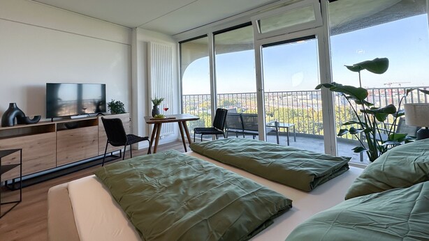 Una habitación de hotel moderna con balcón, televisor de pantalla plana, escritorio de madera y ropa de cama verde.