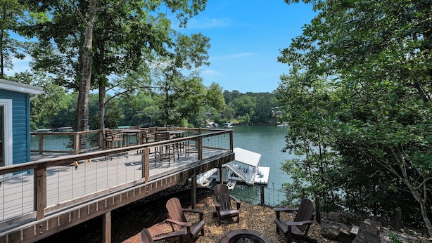 A deck with outdoor seating and a fire pit, overlooking a lake with boats and trees. - Barney’s Bluff - Towing Pontoon + Dock, Pet-Friendly (Crane Hill)