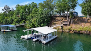 A docked boat with a covered seating area and a small building nearby. - Barney’s Bluff - Towing Pontoon + Dock, Pet-Friendly (Crane Hill)