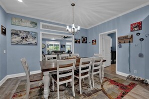 A dining area with a wooden table and white chairs, a chandelier, and artwork on the walls.