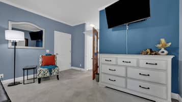 A bedroom with a bed, a dresser, a chair, a lamp, and a TV mounted on the wall.