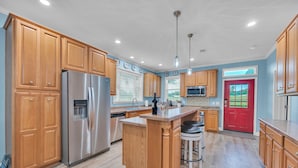 A modern kitchen with wooden cabinets, stainless steel appliances, and a central island with bar stools. - Barney’s Bluff - Towing Pontoon + Dock, Pet-Friendly (Crane Hill)
