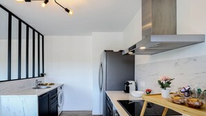 Ett modernt kök med en inbyggd tvättmaskin, ett kylskåp i rostfritt stål och en bänkskiva i trä med en svart induktionshäll.