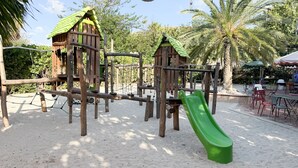 Un parque infantil con juegos de madera y un tobogán verde.