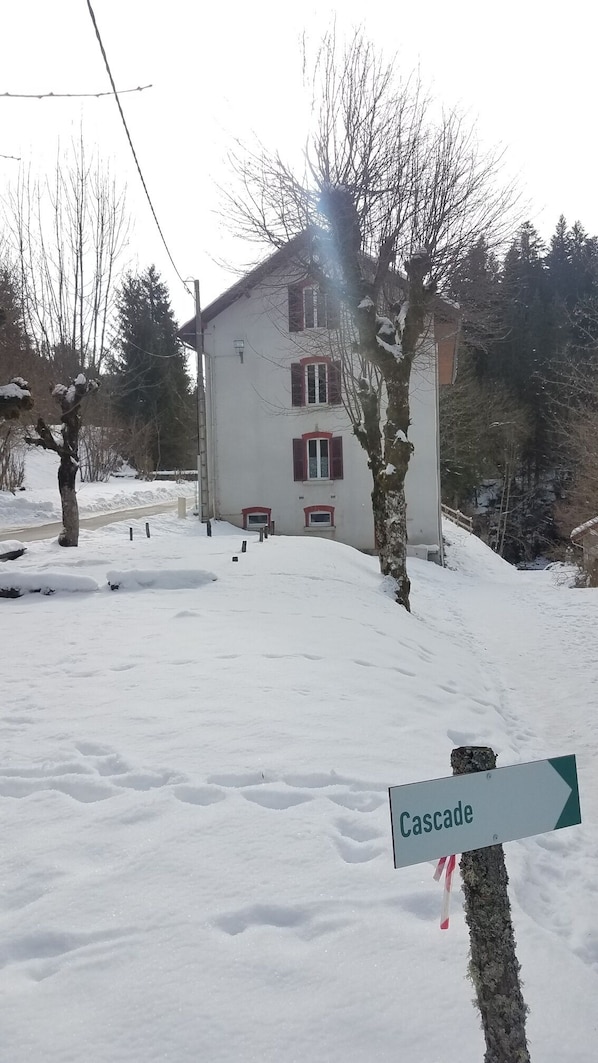 A snow-covered landscape with a white building featuring red window shutters and a sign indicating 'Cascade'.