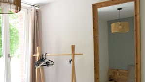 A bedroom with a wooden bed, a large mirror, a wooden drying rack, and a window with curtains. - LE GRAND TETRAS in a charming property in the heart of the Blue Spring area (Montperreux)