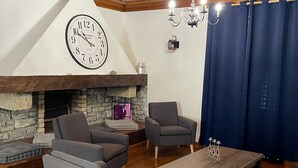 A living room with a stone fireplace, a large clock, and a chandelier. - LE GRAND TETRAS in a charming property in the heart of the Blue Spring area (Montperreux)