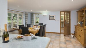 Un coin repas avec une table dressée pour le petit-déjeuner, une bouteille de champagne et une vue sur le jardin par les fenêtres.
