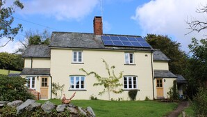 Une maison à deux étages, dotée d’un toit en pente, de panneaux solaires sur le toit et d’un mur de pierre en premier plan.