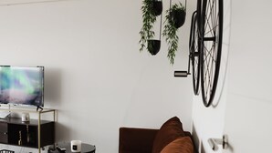 Uma sala de estar moderna com um sofá marrom, uma televisão, uma mesinha e uma bicicleta presa à parede.
