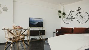 Uma sala moderna com cama, área de jantar com mesa e cadeiras, TV na parede e uma bicicleta pendurada na parede.