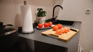 Uma bancada de cozinha com tábua de corte, tomates, dispensador de papel toalha, planta em vaso e uma pia.