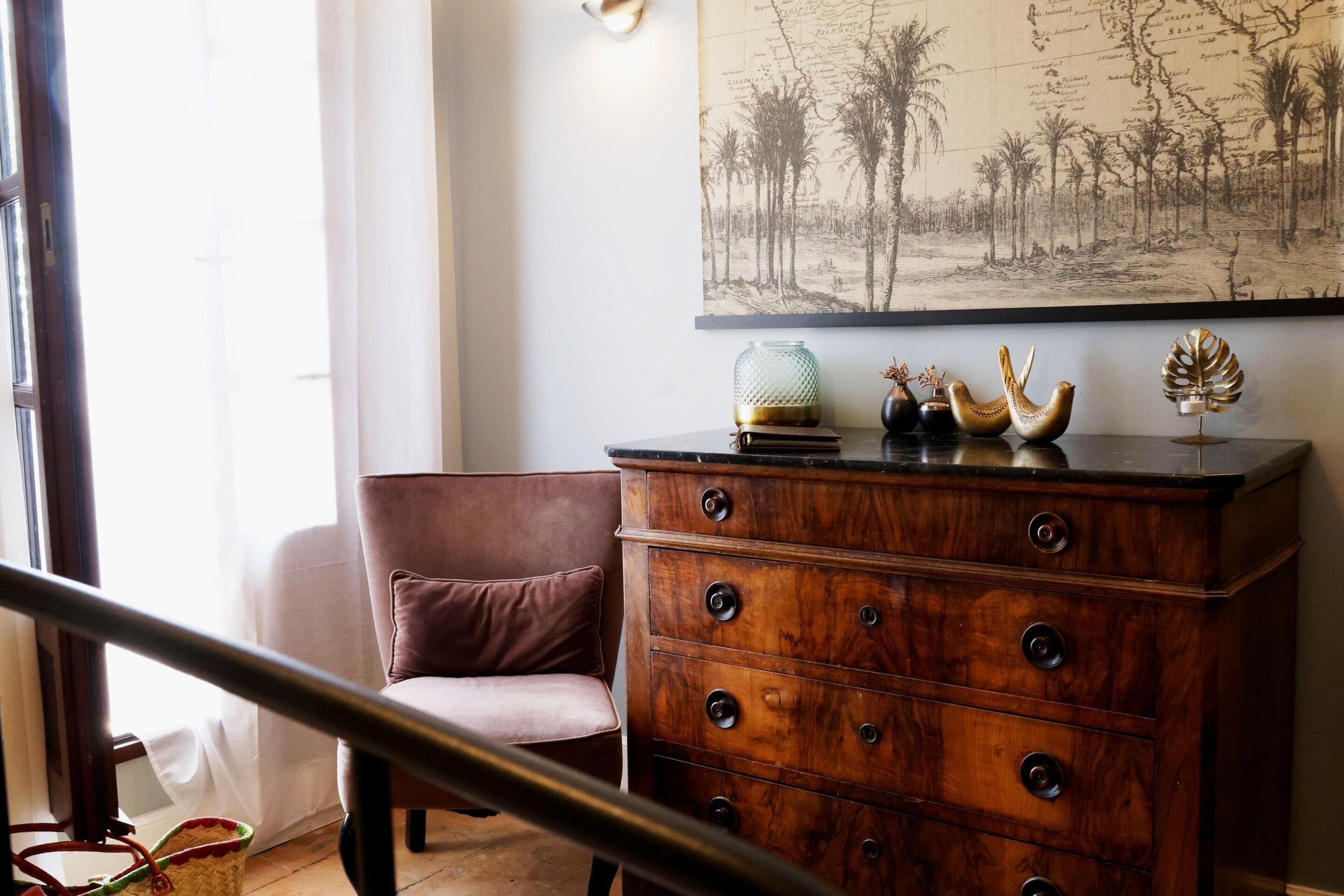 A room with a wooden dresser, a cushioned chair, and a map on the wall.