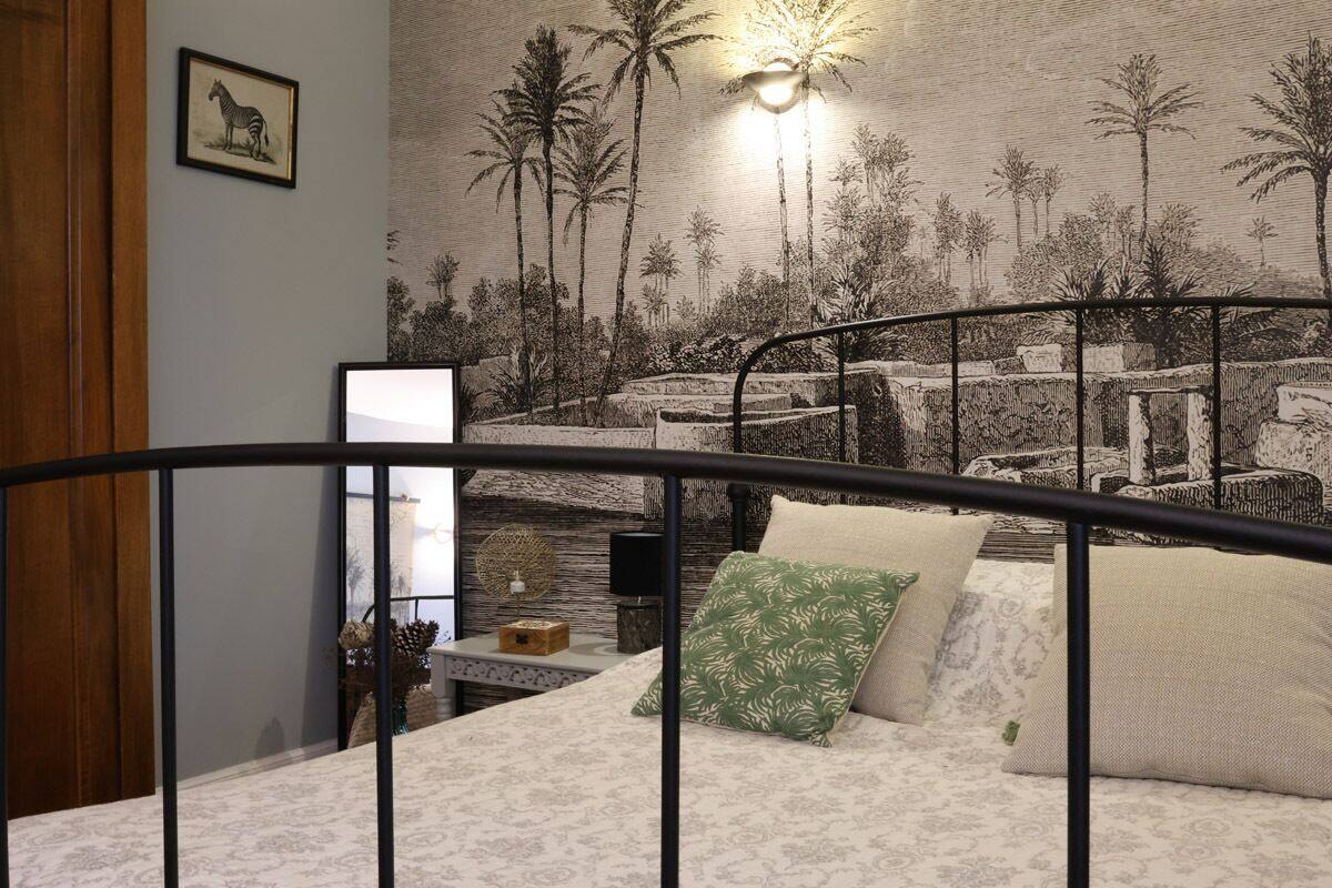 Quarto com cama, mesa de cabeceira, painel decorativo na parede e um quadro emoldurado.