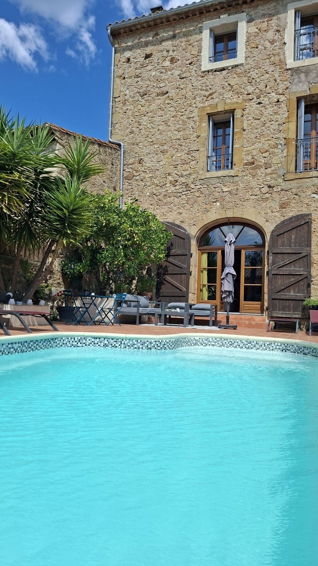 Edifici de pedra amb piscina, seients exteriors i una gran porta de fusta.