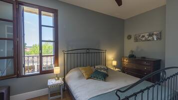 A bedroom with a bed, bedside tables, a dresser, a ceiling fan, and a window with a view.