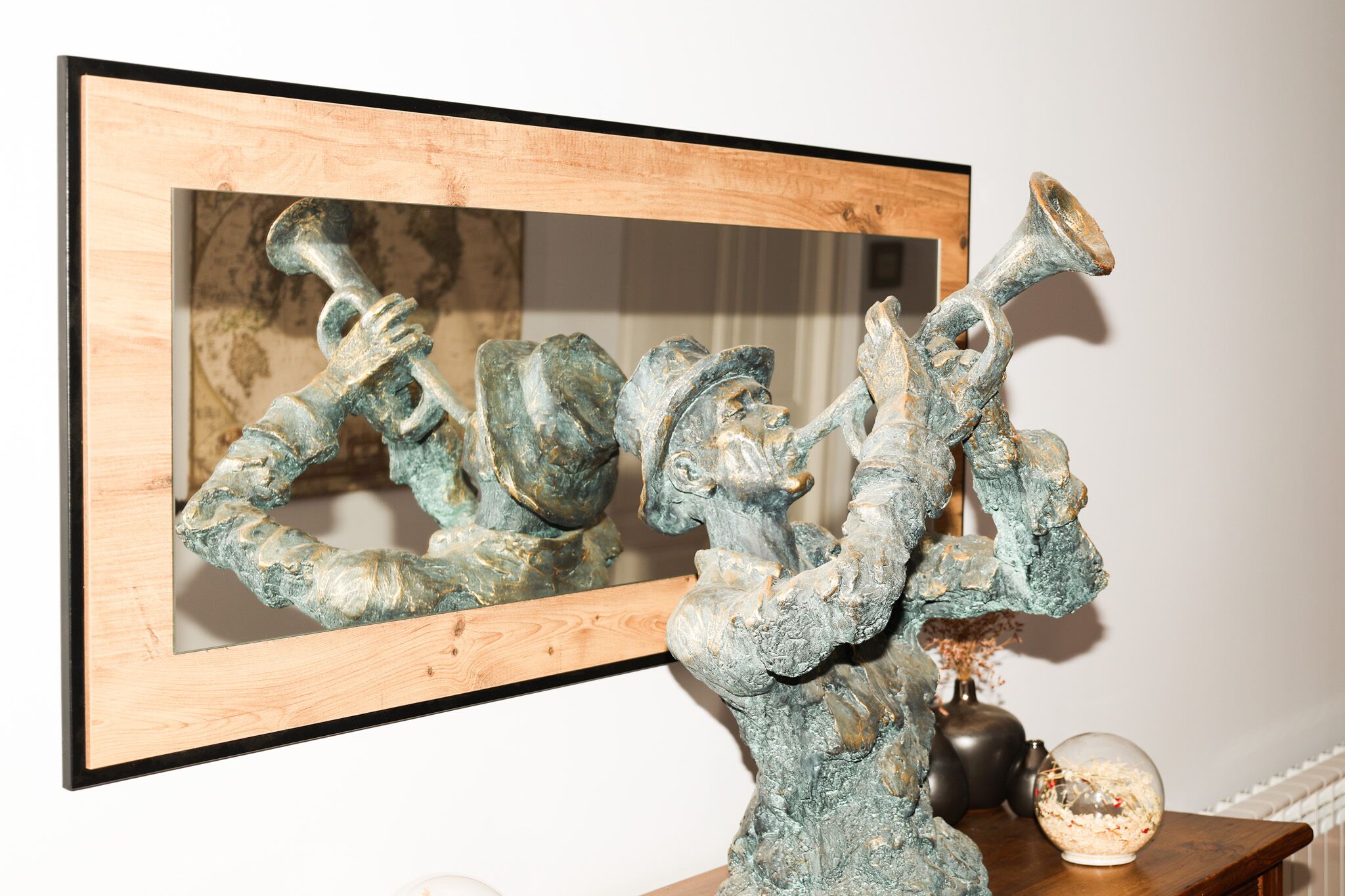 Escultura emoldurada de uma figura tocando trompete, sobre uma mesa de madeira com um vaso e um globo por perto.