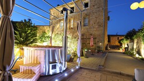 A stone building with a patio area featuring a hot tub, umbrellas, and potted plants. - Maison Dix (Neffies)