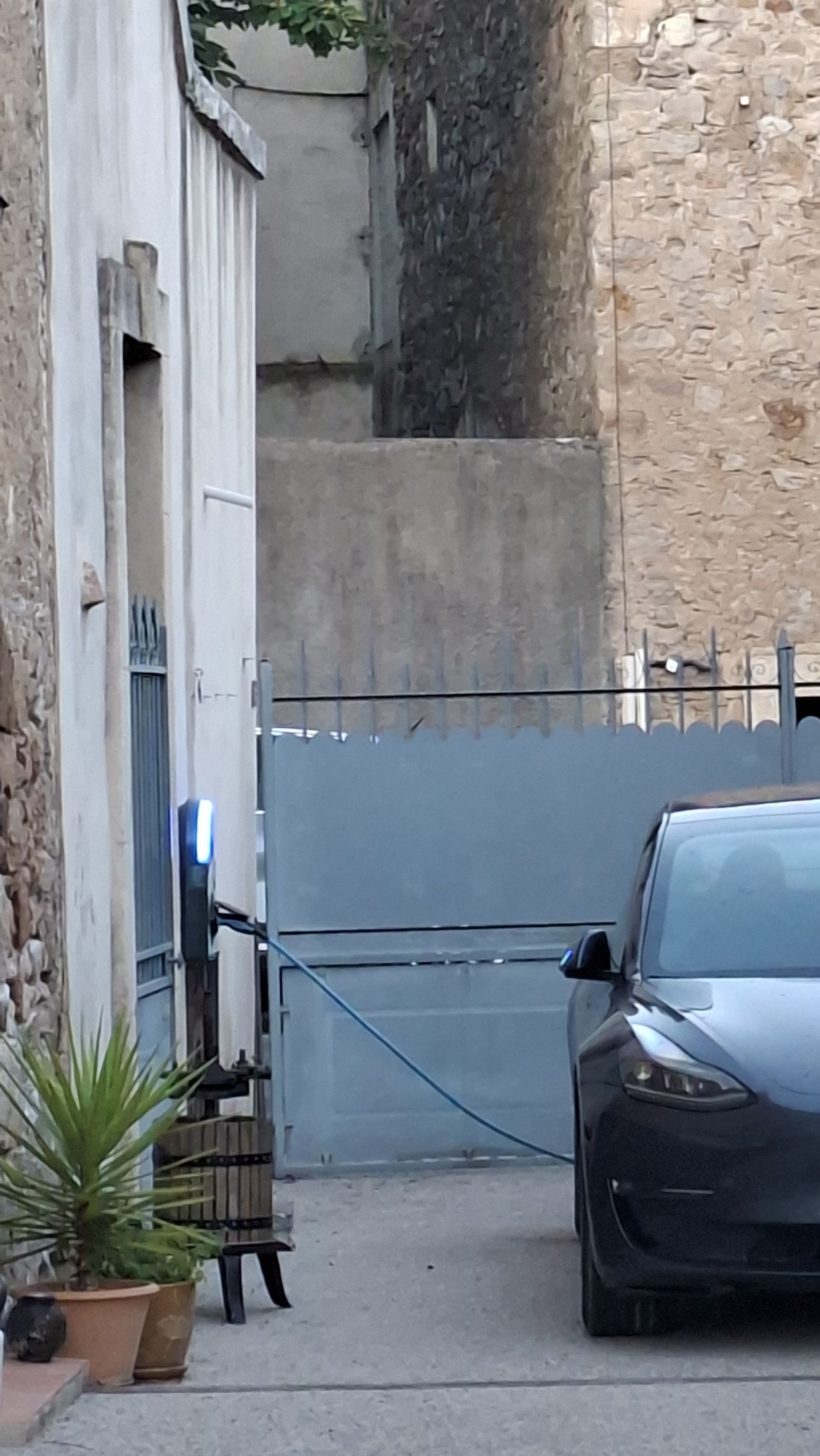 A gated entrance with a car parked inside, a potted plant, and a stone wall.