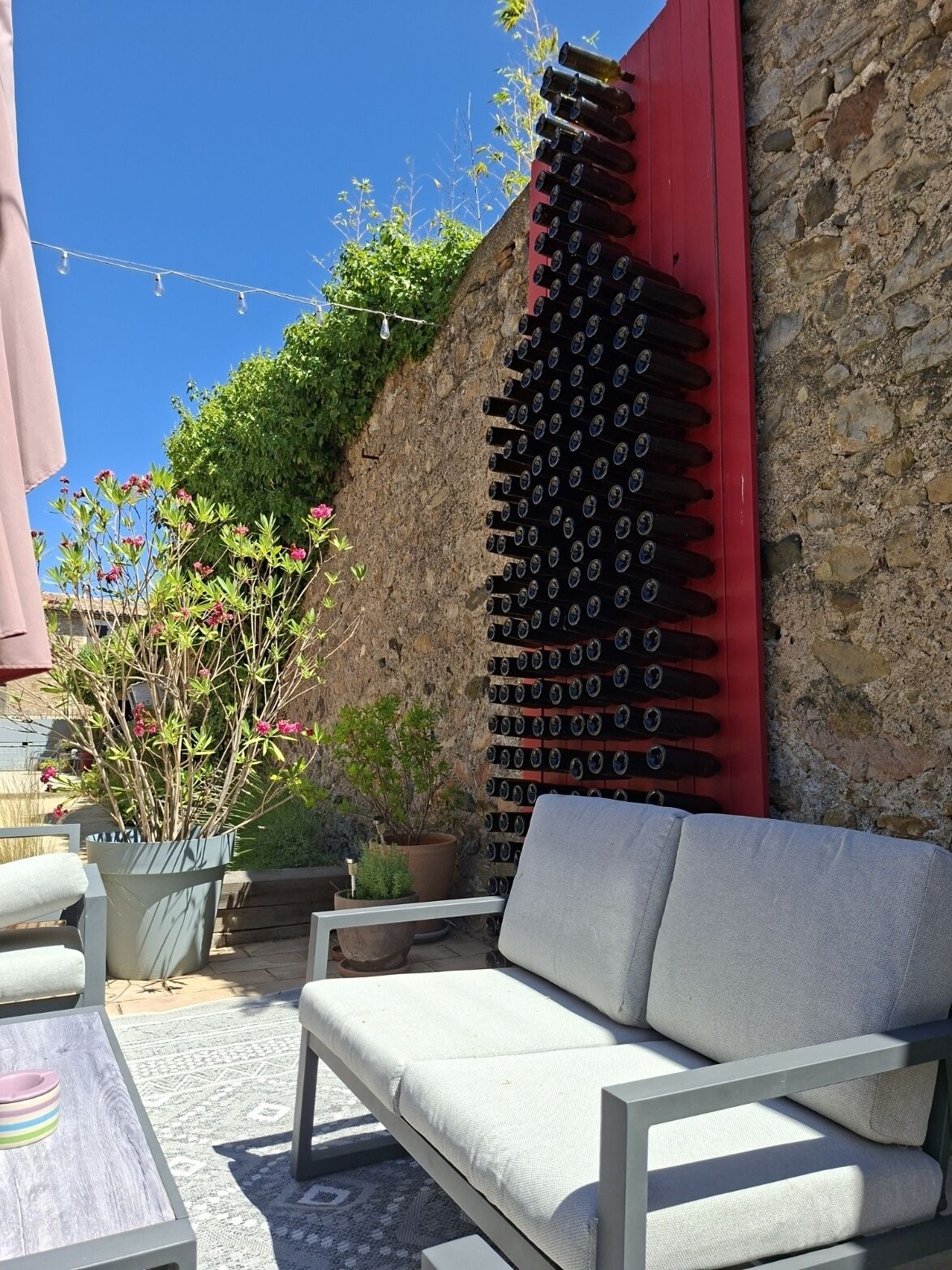 Un patio con un sofá blanco, un muro de piedra y una estantería para vino tinto.