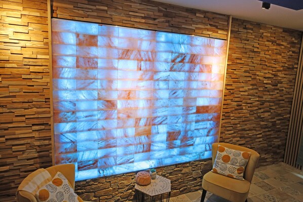 Una habitación con una pantalla grande montada en la pared, dos sillones con cojines estampados y una mesita con un adorno.
