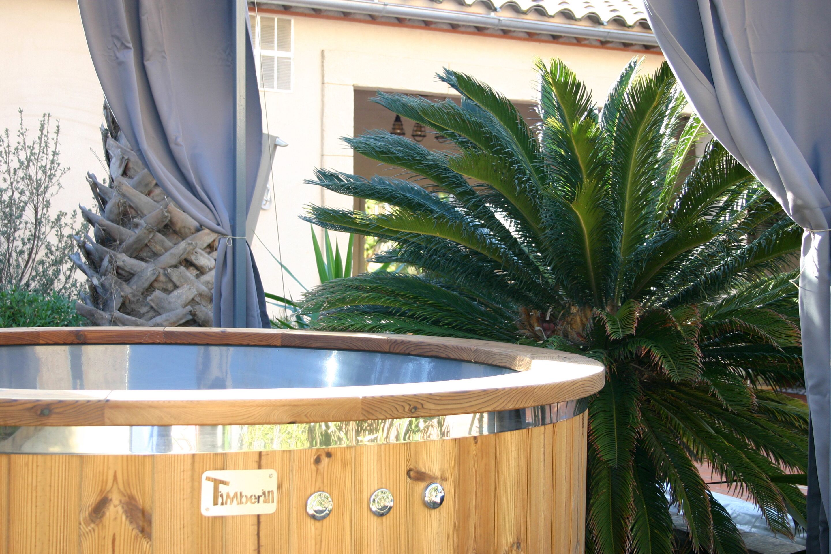 Ein hölzernes Whirlpool mit einem Etikett, umgeben von einer Palme und Vorhängen.