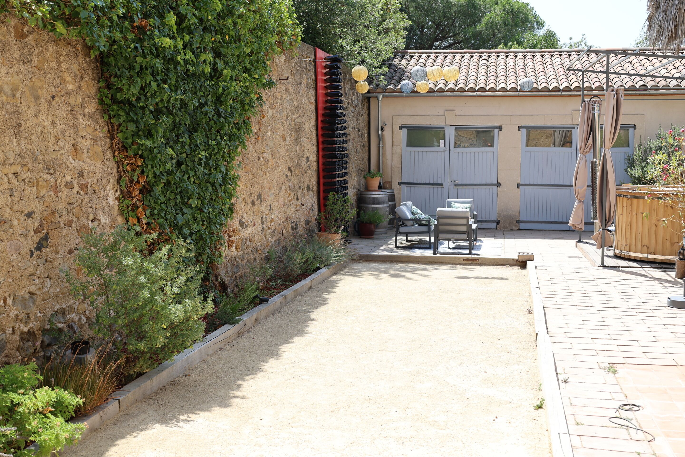Un patio con muro de piedra, una banca y una pérgola con faroles colgantes.