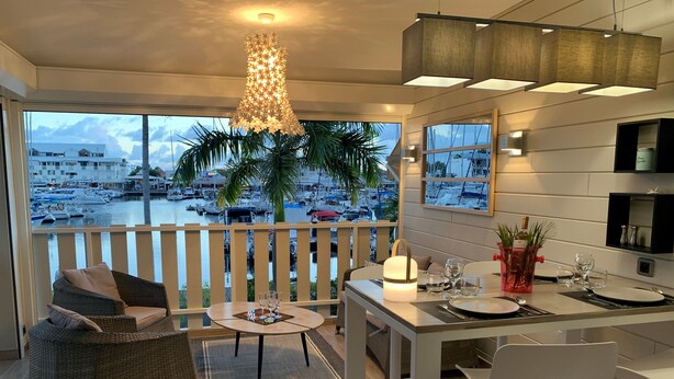A balcony with a view of a marina, a dining table set with glasses and cutlery, and a wicker chair. - MARINA MANZANA, 4* Luxury apartment, exceptional view of the marina (Saint-François)