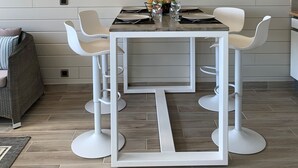 A modern kitchen with a white table, four white bar stools, a large wall clock, and built-in shelves. - MARINA MANZANA, 4* Luxury apartment, exceptional view of the marina (Saint-François)