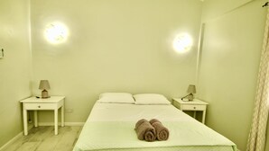 Et hotelværelse med seng, to sengeborde, to lamper, et håndklæde på sengen og en gardin for vinduet.